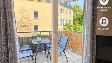 A balcony with a table and chairs, a sliding glass door, and a view of buildings.