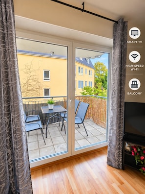 Een balkon met een tafel en stoelen, een schuifdeur en uitzicht op gebouwen.