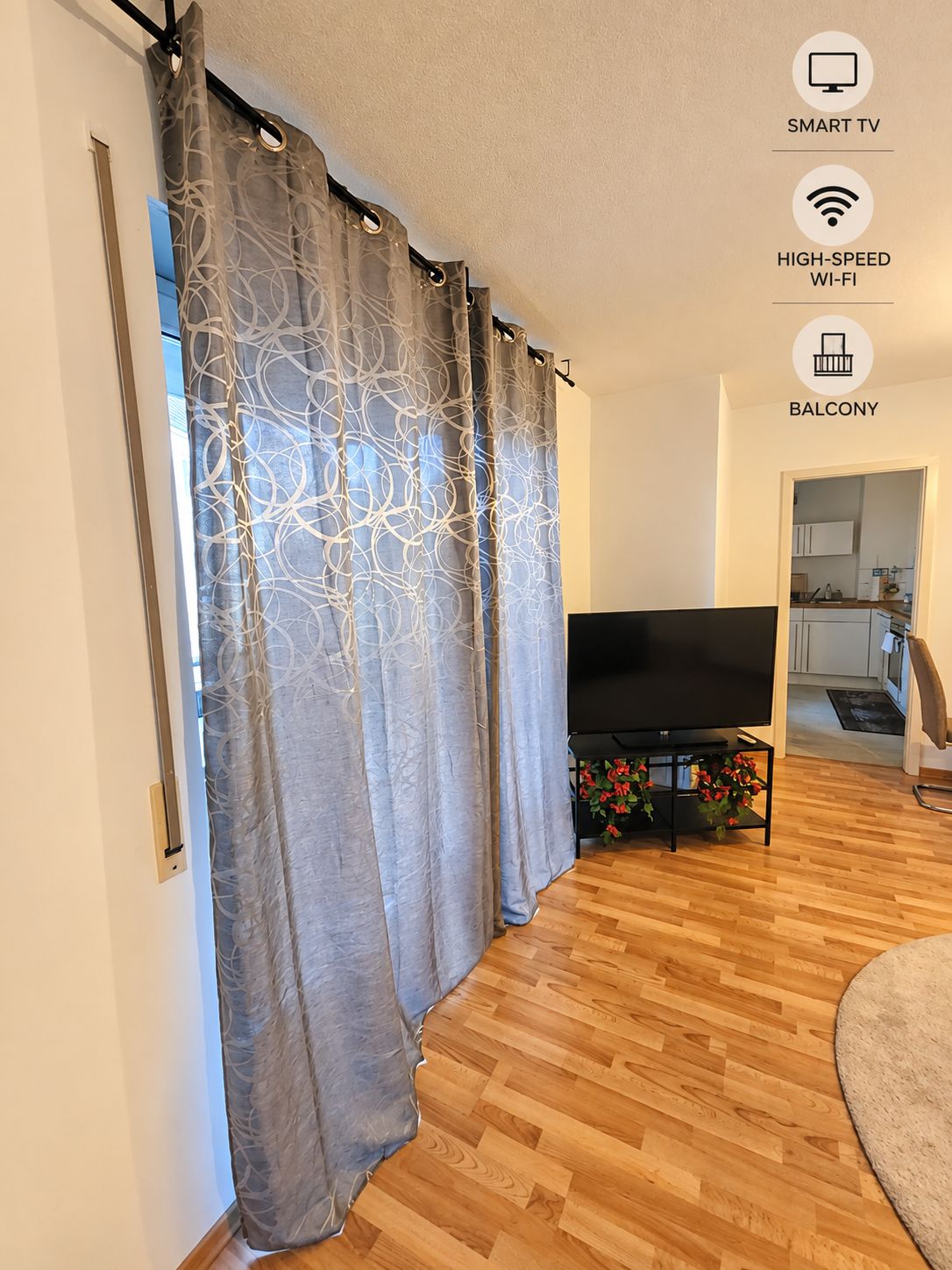Ein Wohnzimmer mit Flachbildfernseher, Holzböden und einem Balkon.