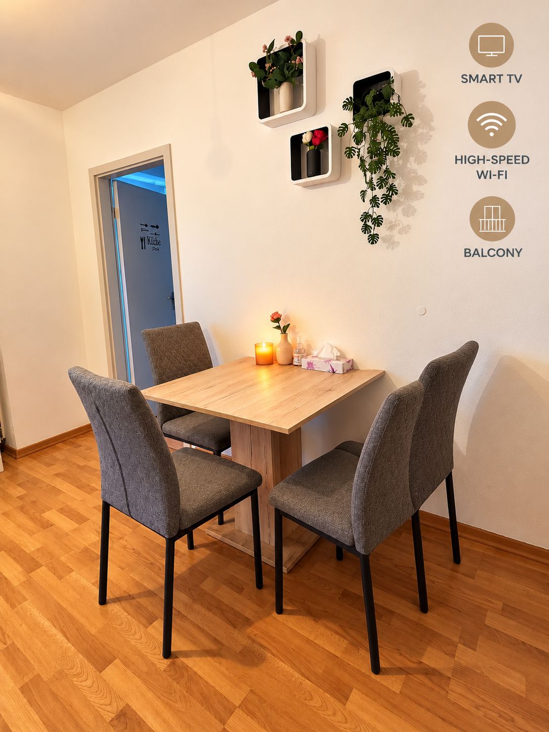 Un área de comedor con una mesa de madera y cuatro sillas grises, una planta pequeña en la pared y una vela sobre la mesa.