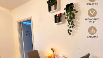Un área de comedor con una mesa de madera y cuatro sillas grises, una planta pequeña en la pared y una vela sobre la mesa.