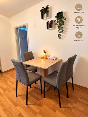 Un coin repas avec une table en bois et quatre chaises grises, une petite plante accrochée au mur et une bougie posée sur la table.