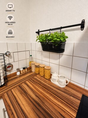 Une cuisine avec un plan de travail en bois, un pot à suspendre pour plantes et une tasse blanche sur laquelle est inscrit « ZUCKER MILK ».