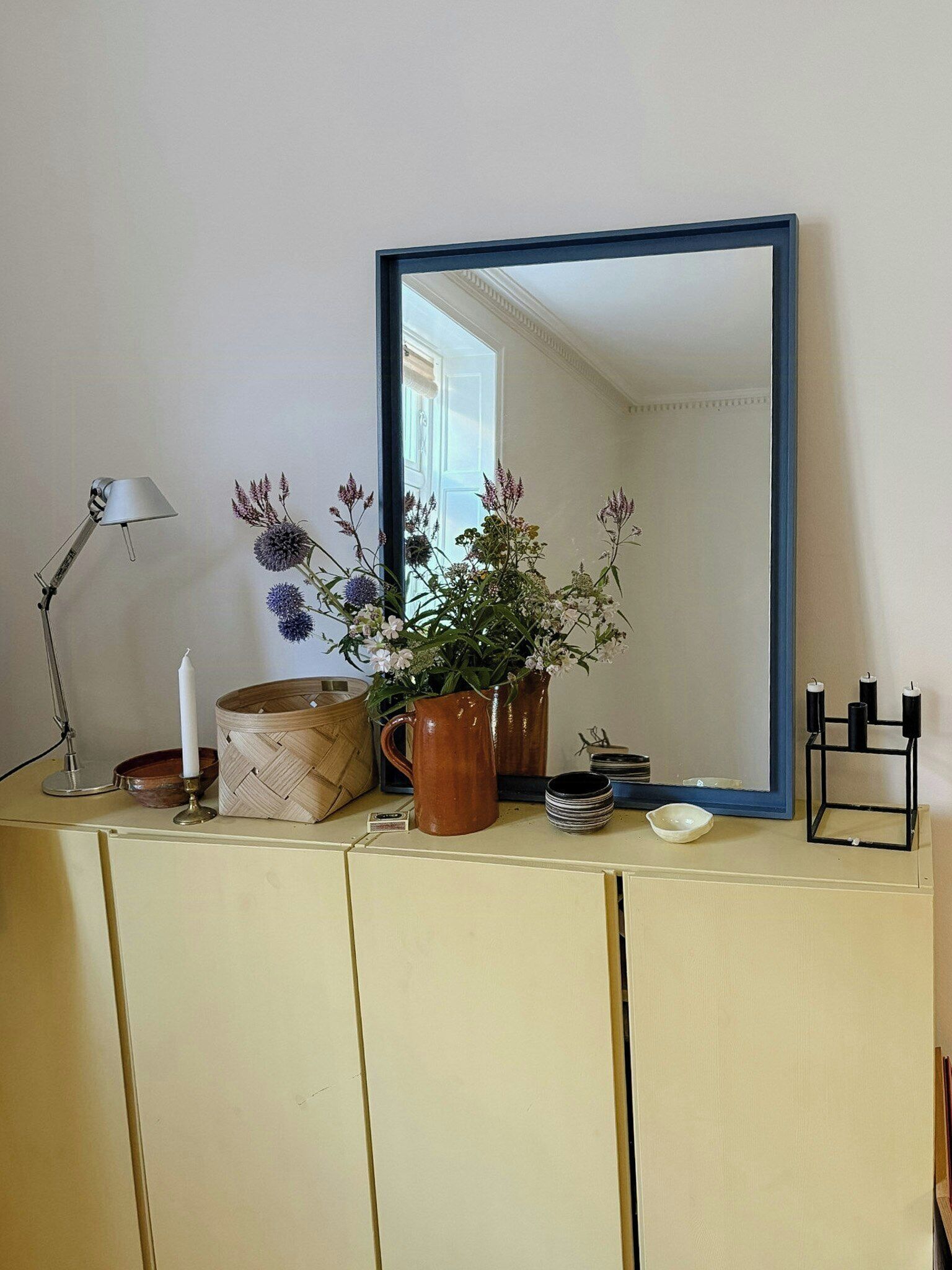 A room with a mirror, a lamp, a vase with flowers, a candle, and a small table with dishes.