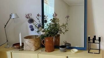 A room with a mirror, a lamp, a vase with flowers, a candle, and a small table with dishes.