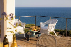 A terrace with two wicker chairs, a table with a fruit bowl, and a view of the sea. - TRULLO EXCLUSIVE (Torre Vado)