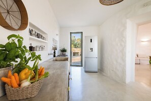 A kitchen with a white countertop, a basket of vegetables, and a view of the outside. - TRULLO EXCLUSIVE (Torre Vado)