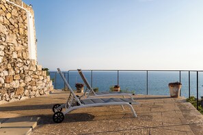 A balcony with a stone wall, a metal chair, and potted plants overlooking the sea. - TRULLO EXCLUSIVE (Torre Vado)