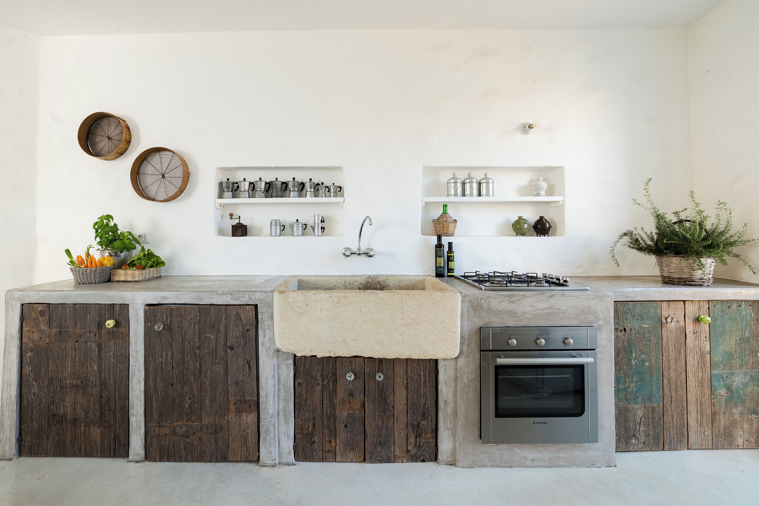 A kitchen with a built-in stove, oven, and sink. There are shelves with kitchenware and a potted plant.