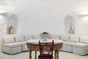 A room with a white curved sofa, a wooden table with a bowl of fruit, and two vases on the walls. - TRULLO EXCLUSIVE (Torre Vado)