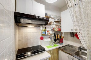 Een kleine keuken met witte kastjes, een zwarte afzuigkap en een RVS spoelbak.