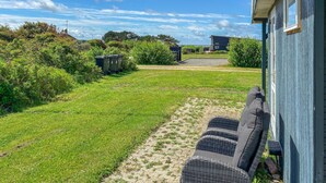 A grassy yard with a paved path, a blue building, and a black trash bin. - Gorgeous home in Vestervig with WiFi (Vestervig)