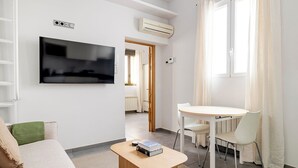 A modern living room with a flat-screen TV, a dining table with chairs, a sofa, and an air conditioning unit. - Design and Comfort in Prosperity (Madrid)