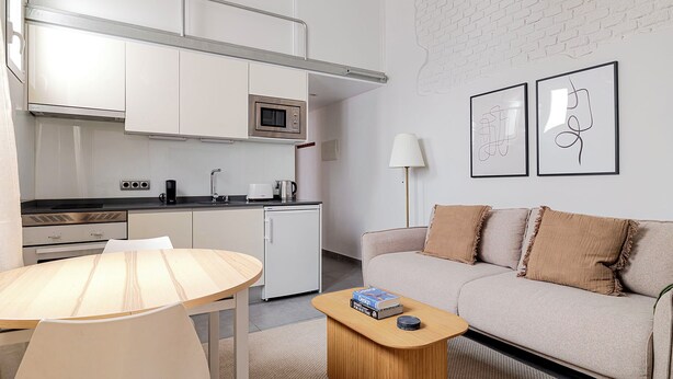 A modern kitchen with white cabinets, a microwave, and a coffee maker. There is a dining table with a lamp, a sofa with cushions, and two framed artworks on the wall. - Design and Comfort in Prosperity (Madrid)