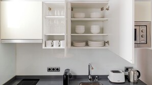 A kitchen with a built-in cabinet containing white mugs, glasses, bowls, and plates. - Design and Comfort in Prosperity (Madrid)