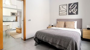 A modern bedroom with a bed, bedside tables, a nightstand, a wall-mounted artwork, and a view into the adjacent kitchen. - Design and Comfort in Prosperity (Madrid)
