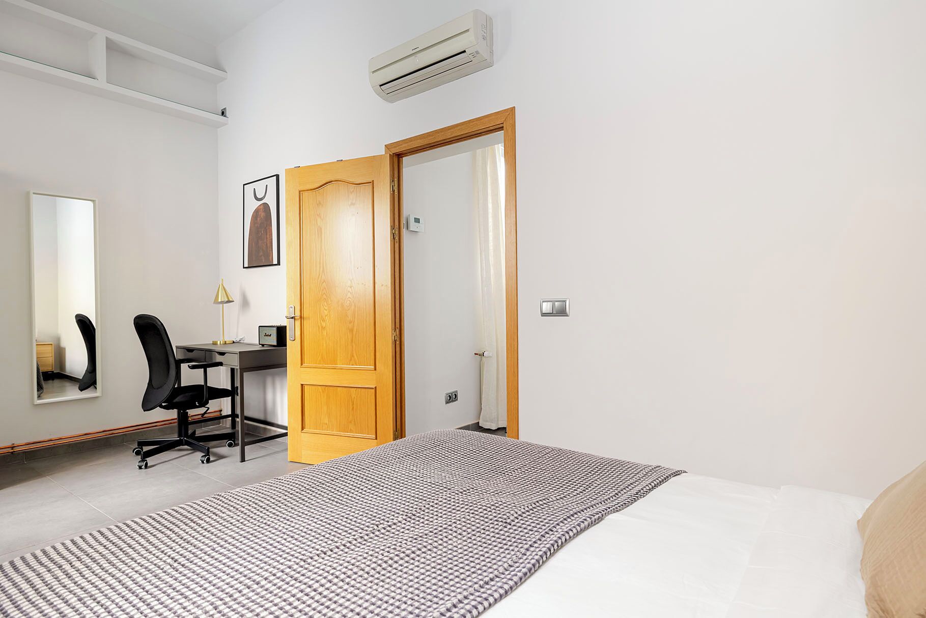 Un dormitorio con cama, un escritorio con silla, un espejo y una puerta.