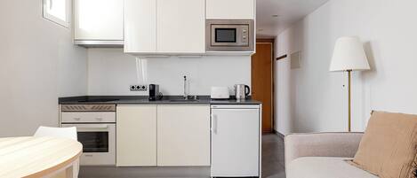Una kitchenette compacta con microondas, cafetera y tostadora, un refrigerador pequeño y un área de comedor con mesa y sofá.