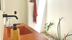A bathroom with a wooden sink, a black faucet, a glass jar, a towel hanging on a hook, and a small plant. - Kasa Koh  (Brisas de Zicatela)