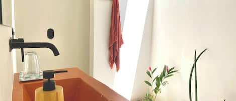 A bathroom with a wooden sink, a black faucet, a glass jar, a towel hanging on a hook, and a small plant.
