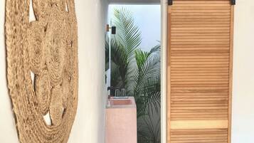 A room with a bed, a wall-mounted woven artwork, a sliding wooden door, and a view of a balcony with plants.