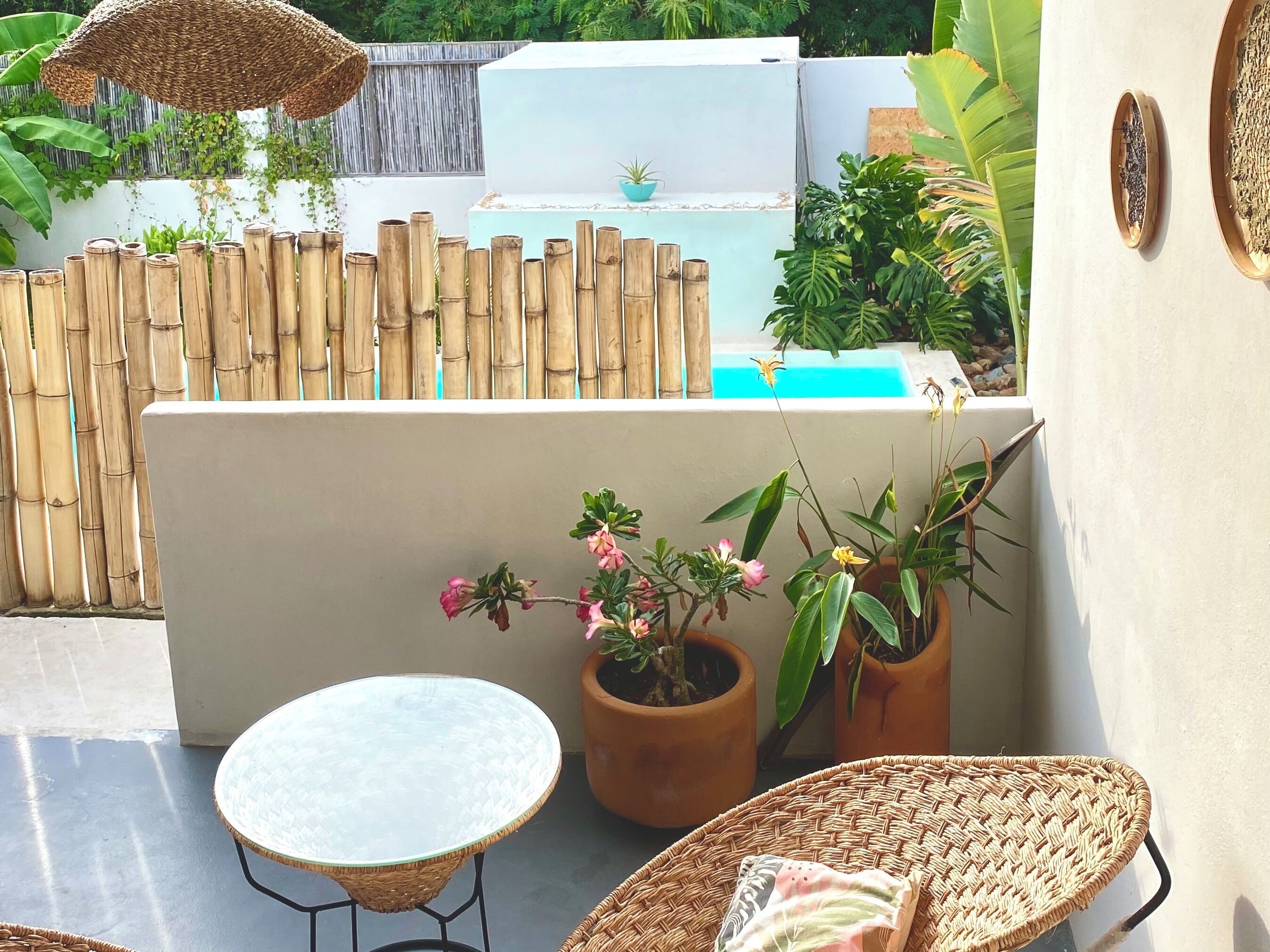 A patio area with a round glass table, wicker chairs, potted plants, and a bamboo fence.