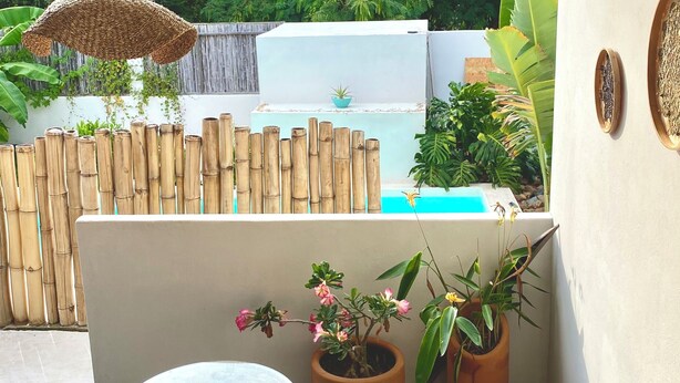 A patio area with a round glass table, wicker chairs, potted plants, and a bamboo fence. - Kasa Koh  (Brisas de Zicatela)