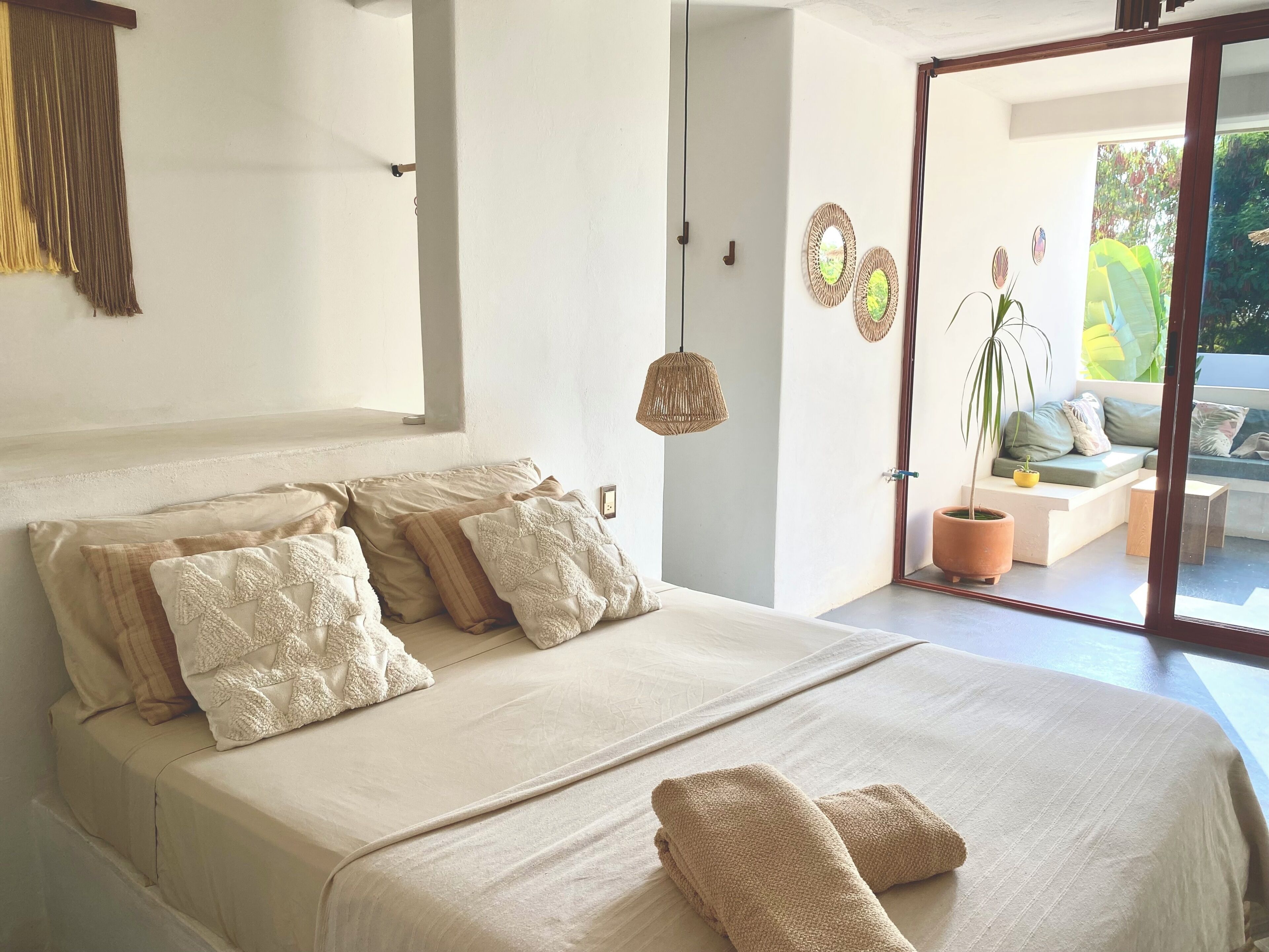 A bedroom with a large bed, a view of the outdoor seating area, and a hanging light fixture.