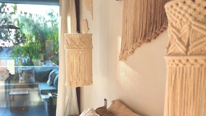 A room with a sofa, a hanging macrame wall decoration, and a view through a window. - Kasa Koh  (Brisas de Zicatela)