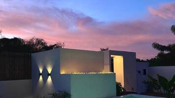A modern outdoor pool area with a clear pool, a low wall with integrated lighting, and a sunset sky.