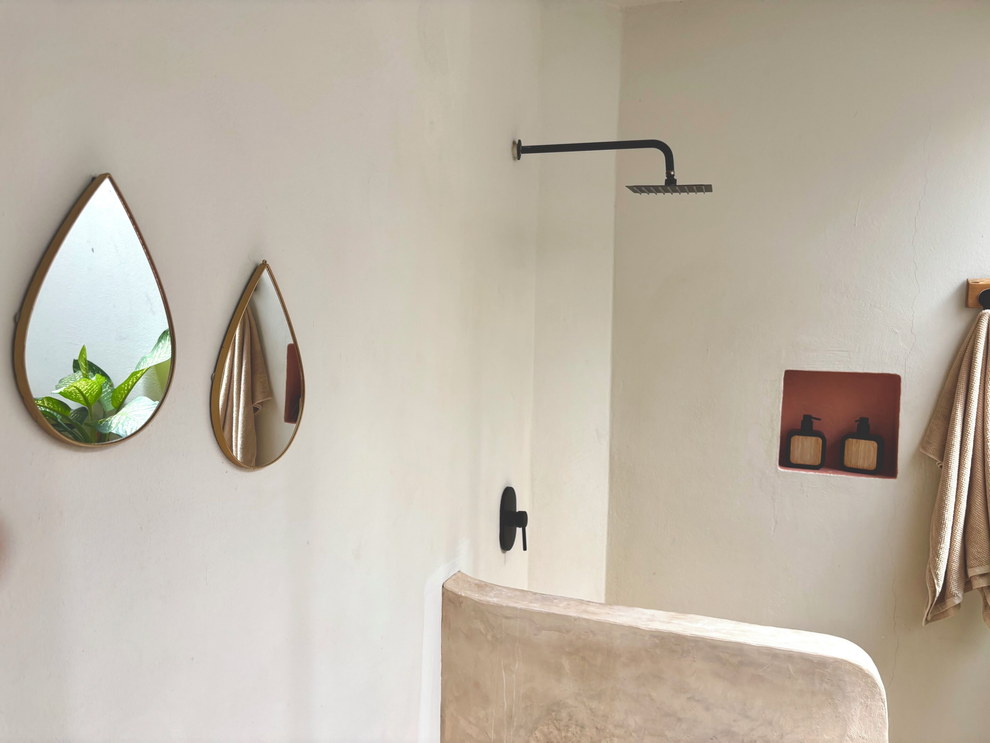 A bathroom with a shower, two wall-mounted mirrors, a towel rack, and a soap dispenser.