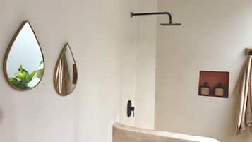 A bathroom with a shower, two wall-mounted mirrors, a towel rack, and a soap dispenser.
