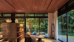 A modern interior with a wooden ceiling, large windows, a stone fireplace, and a seating area with a round table.
