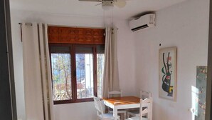 A room with a dining table, chairs, a ceiling fan, a bed, and a window with curtains.