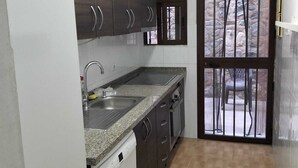 A compact kitchen with dark wooden cabinets, a white refrigerator, a granite countertop, and a window with metal bars.