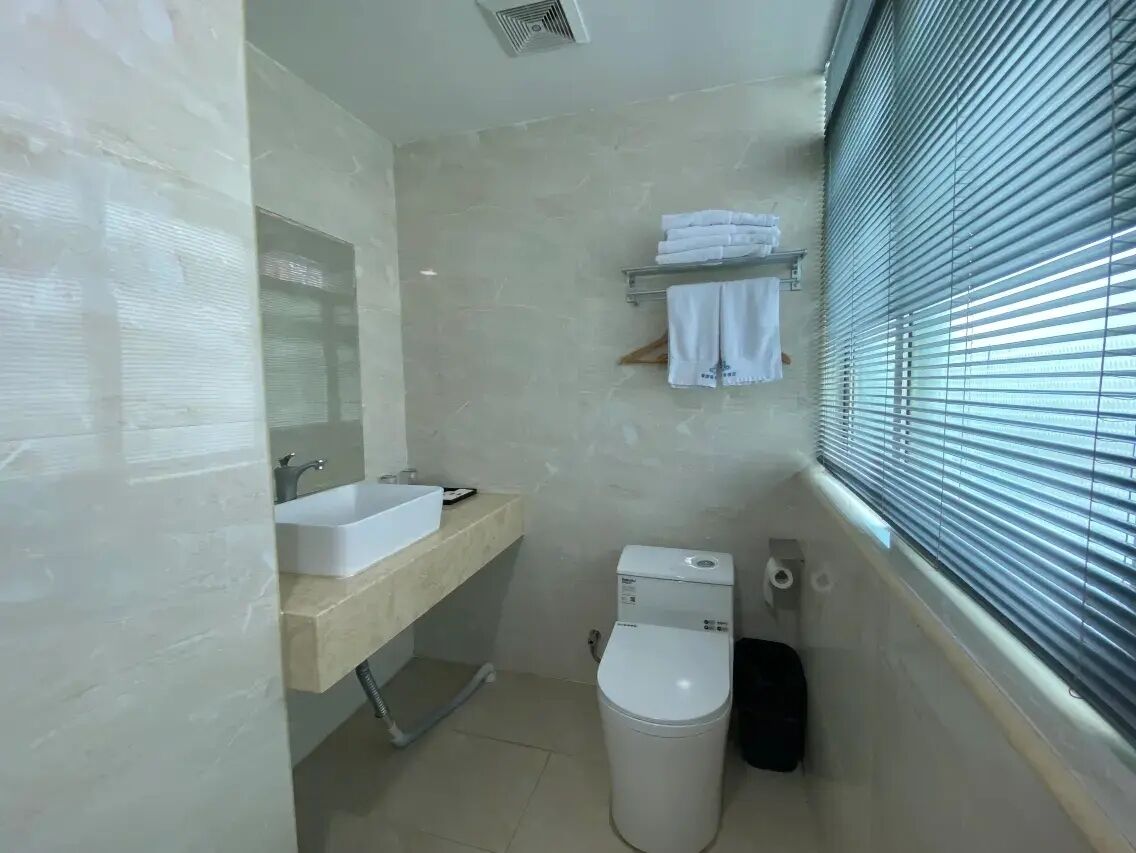 Casa de banho com lavatório branco, espelho, sanita e janela com persianas.