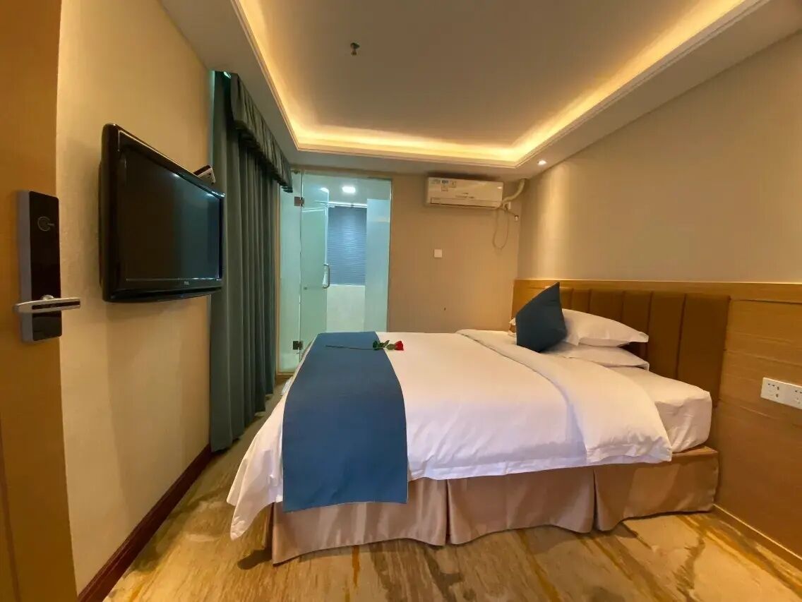 A hotel room with a bed, a TV, an air conditioning unit, and a door leading to a bathroom.