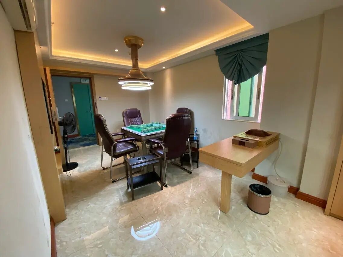 A room with a dining table, chairs, a ceiling fan, a window with curtains, and a trash bin.