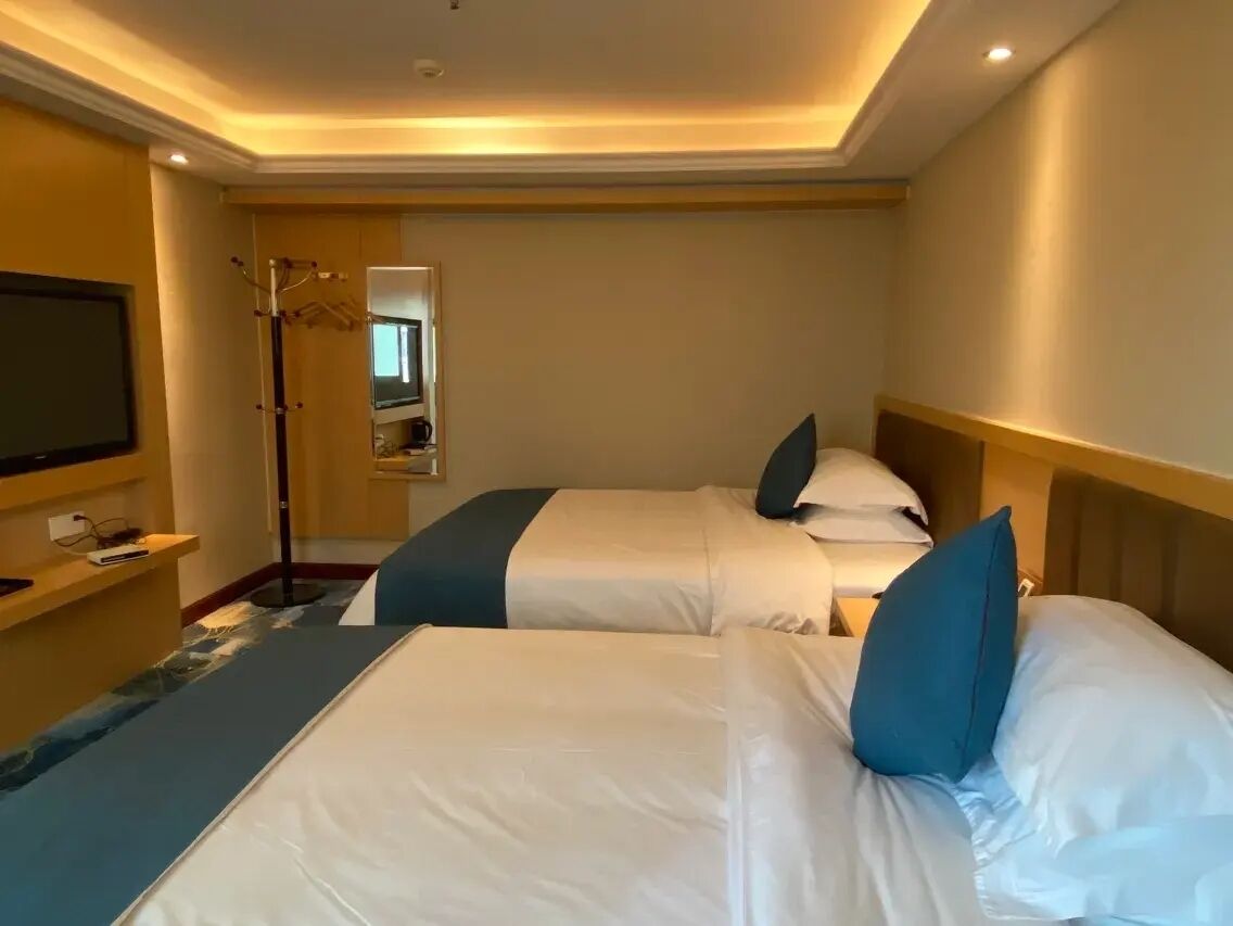 Una habitación de hotel con dos camas, un televisor de pantalla plana, un perchero y un espejo.