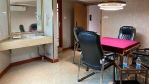 A hotel room with a bathroom, a dining table with two chairs, a red tablecloth, and a ceiling light fixture.