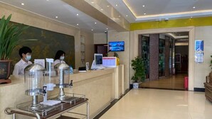 A hotel reception area with a counter, a digital screen, and a potted plant.