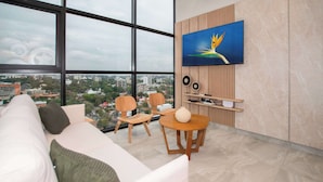 A modern living room with a large window, a sofa, two chairs, a round table, and a mounted TV. - Corporate Stays Matrisa - 405 (Asunción)