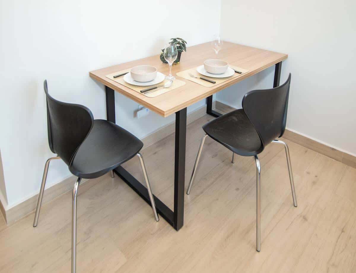 Una mesa de comedor con dos sillas negras, una pequeña planta en maceta y una copa de vino.