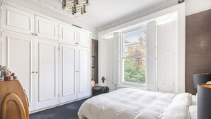 A bedroom with a large bed, a window with a view of the outside, and white cabinetry. - The Mid-Century Modern Maisonette, by Veeve (London)