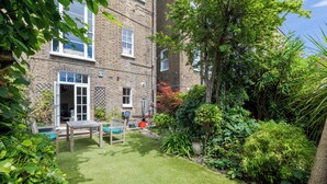 A brick building with a small lawn, a wooden bench, and potted plants. - The Mid-Century Modern Maisonette, by Veeve (London)