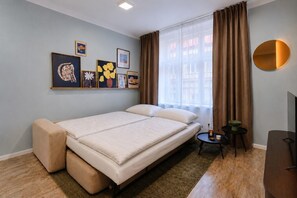 Una camera da letto con un letto, un tavolino con una ciotola, una sedia, uno specchio rotondo e opere d'arte appese al muro.