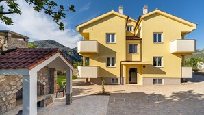 A two-story yellow building with a stone facade, a covered patio, and a mountainous backdrop. - Cozy apartment in Starigrad Paklenica with WiFi (Starigrad Paklenica)