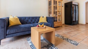 Una sala de estar con un sofá azul, un mueble de madera y un refrigerador negro.
