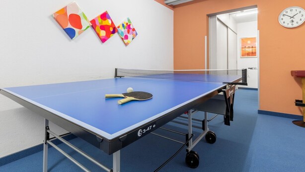 Una mesa de ping pong con una paleta y una pelota, un reloj y arte abstracto en la pared.