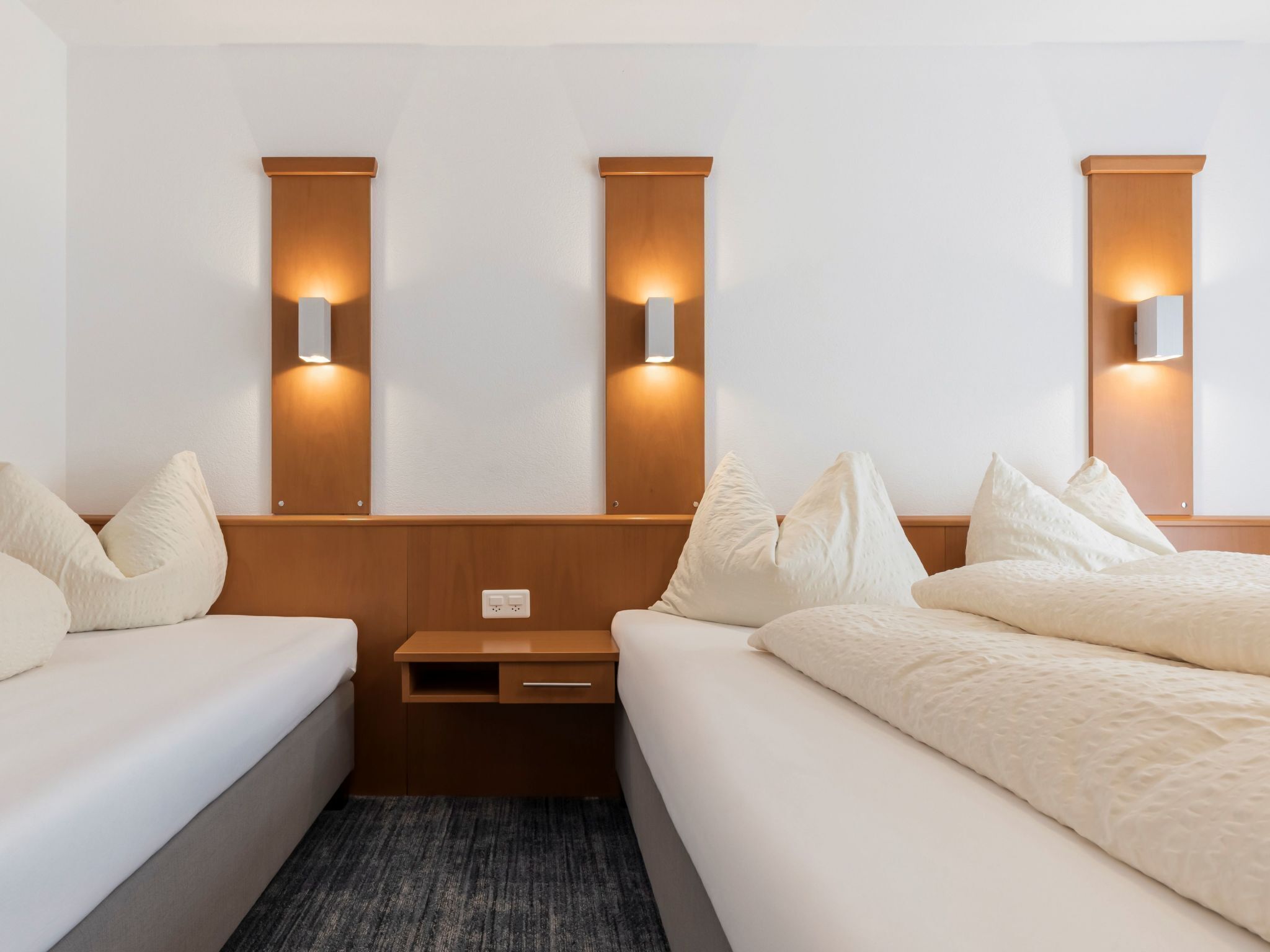 Una habitación de hotel con dos camas, una mesita de noche e iluminación instalada en la pared.